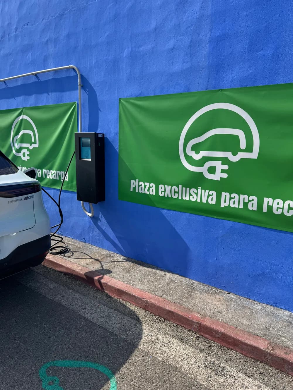 Las dos plazas exclusivas de recarga señalizadas con lonas verdes, con el poste de carga en medio